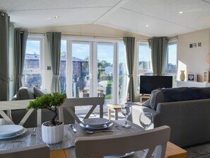 Ein Wohnzimmer mit Esstisch, Stühlen, einer Couch, einem Fernseher und Blick ins Freie.