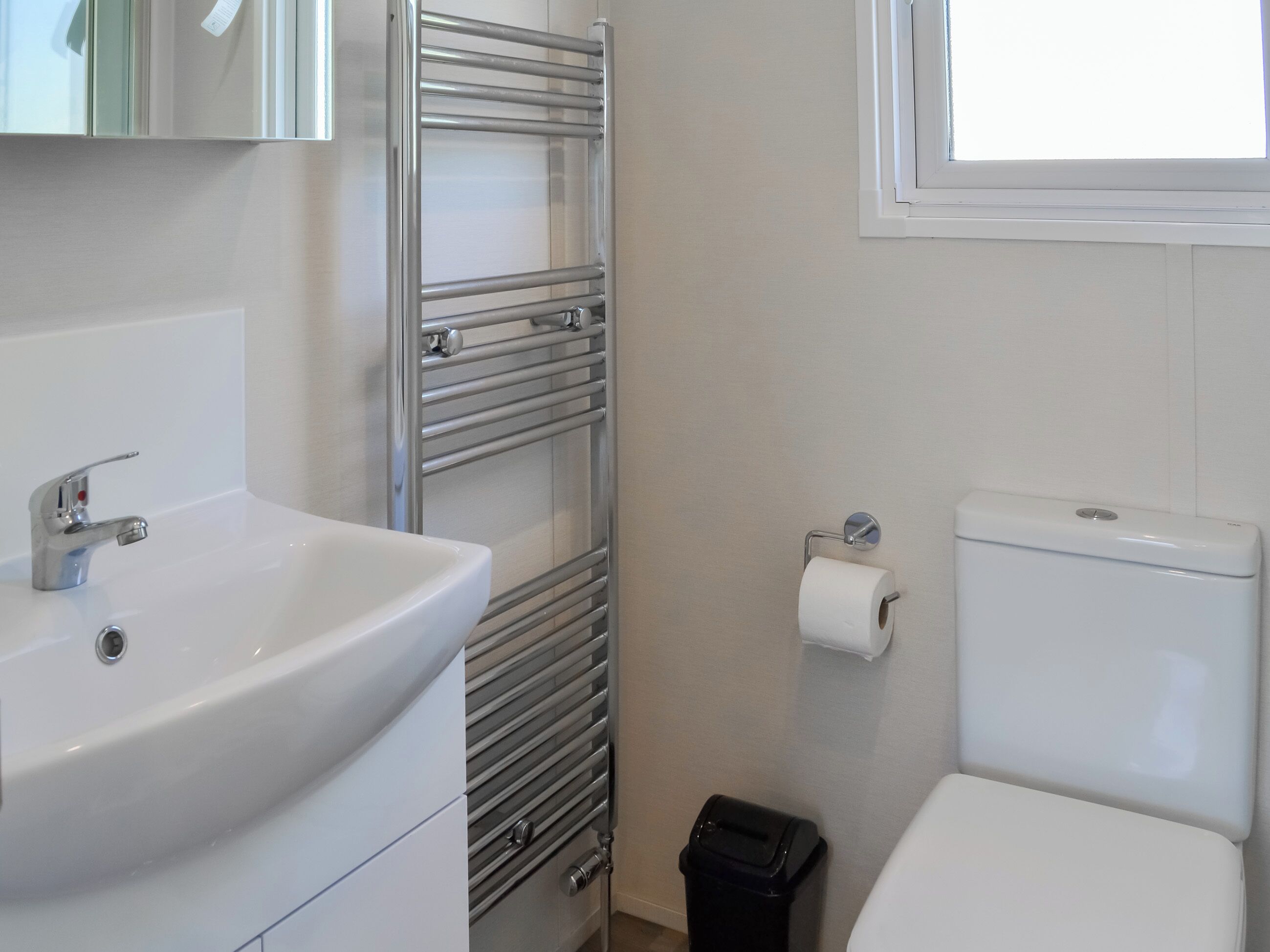 A bathroom with a sink, toilet, towel rack, and a trash bin.