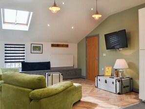 Un salon chaleureux avec un canapé vert, une porte en bois, un téléviseur et une lampe sur une table.