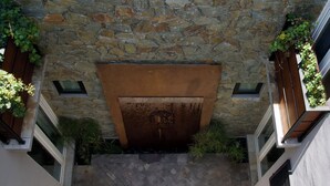 A stone facade with a metal door, a stone wall, and a small garden area with plants. - CASA XANTHE (San Miguel de Allende)