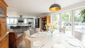 Un coin repas avec une table ronde dressée pour six personnes, entourée de chaises, et une grande fenêtre offrant une vue sur l’extérieur.
