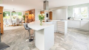 Une cuisine moderne dotée d’un îlot central, de meubles blancs et d’une grande fenêtre qui laisse entrer la lumière naturelle.
