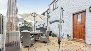 A patio with a grill, outdoor furniture, and a white building with a wooden door. - The Granary - UK41502 (Hundleton, near Pembroke)