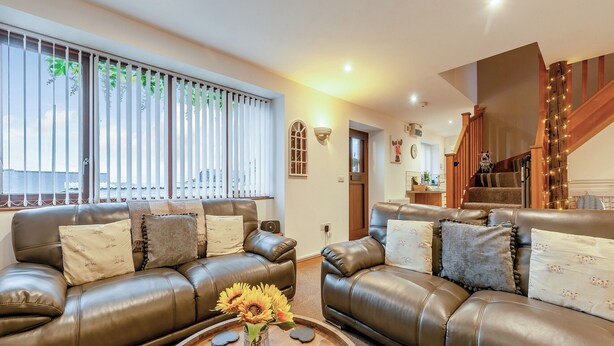 A living room with leather sofas, a coffee table with a vase of flowers, and a staircase with string lights. - The Granary - UK41502 (Hundleton, near Pembroke)