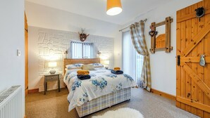 A bedroom with a bed, a nightstand, a lamp, a wooden door, and a white radiator. - The Granary - UK41502 (Hundleton, near Pembroke)
