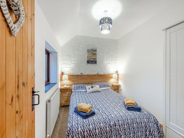 Une chambre à coucher avec une tête de lit en bois, une couvre-lit à motifs, deux lampes de chevet et un luminaire fixé au mur.