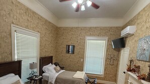 A room with two beds, a ceiling fan, a fireplace, and a television mounted on the wall.