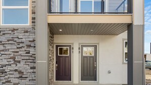 A modern two-story building with a stone facade, two doors, and a covered entrance. - Air Conditioned » Garage » 2BR Townhouse » Sleep 5 (Calgary)