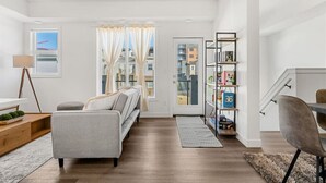 A modern living room with a sofa, a coffee table, a bookshelf, and a dining area with a chair. - Air Conditioned » Garage » 2BR Townhouse » Sleep 5 (Calgary)