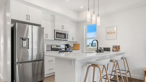 A modern kitchen with stainless steel appliances, white cabinetry, and a large island with bar stools. - Air Conditioned » Garage » 2BR Townhouse » Sleep 5 (Calgary)