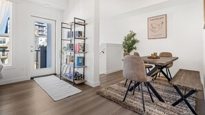 A modern living room with a dining area, featuring a bookshelf, a dining table with chairs, and a framed artwork on the wall. - Air Conditioned » Garage » 2BR Townhouse » Sleep 5 (Calgary)