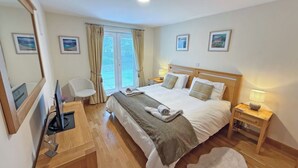 A hotel room with a bed, bedside tables, a desk with a computer, a chair, and a large mirror. - No.4 The Links Apartments (Brora)