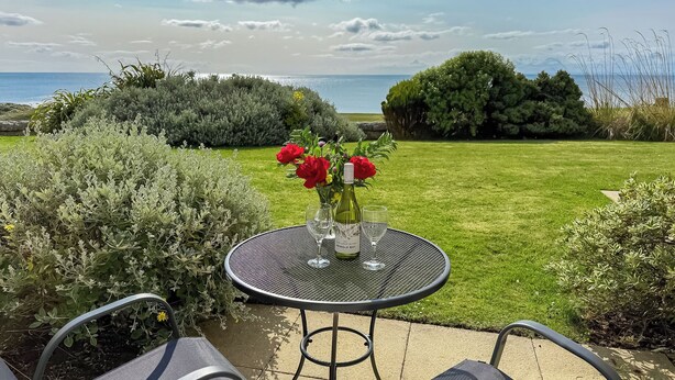 A patio with a table and chairs, a vase with red flowers, and a view of the sea. - No.4 The Links Apartments (Brora)
