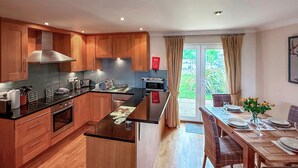 A modern kitchen with wooden cabinets, a central island, and a dining area with a table and chairs. - No.4 The Links Apartments (Brora)