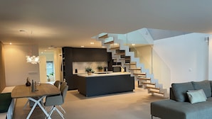A modern kitchen with a central island, a dining area with a table and chairs, and a staircase leading to an upper level. - Copenhagen Residence | Holiday home with Scandinavian flair | View of the water. (Harderwijk)