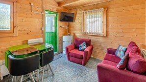 Interior acogedor de una cabaña con paredes de madera, una puerta verde, una mesa de comedor con sillas, un sofá rojo y un televisor montado en la pared.