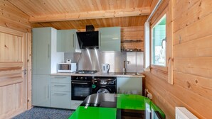 Cocina compacta con paredes de madera, microondas, estufa y pileta.