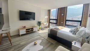Une chambre d’hôtel moderne dotée d’un grand lit, d’un téléviseur fixé au mur, d’un bureau et offrant une vue sur la ville grâce à de grandes fenêtres.