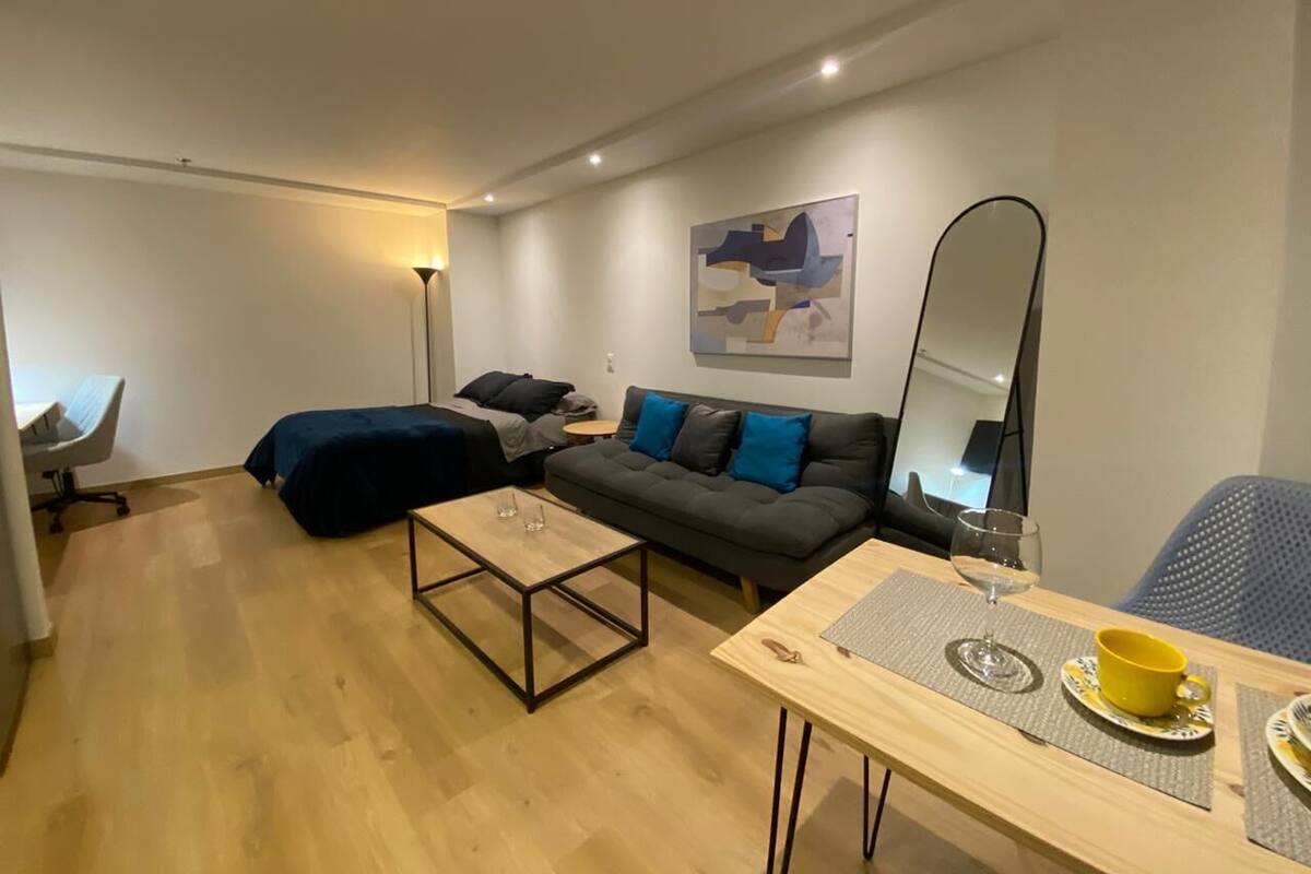 A modern living room with a sofa, a coffee table, a dining table with a yellow cup, and a lamp.