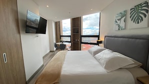 Une chambre d’hôtel moderne dotée d’un grand lit, d’un téléviseur fixé au mur et offrant une vue sur la ville grâce à une grande fenêtre.