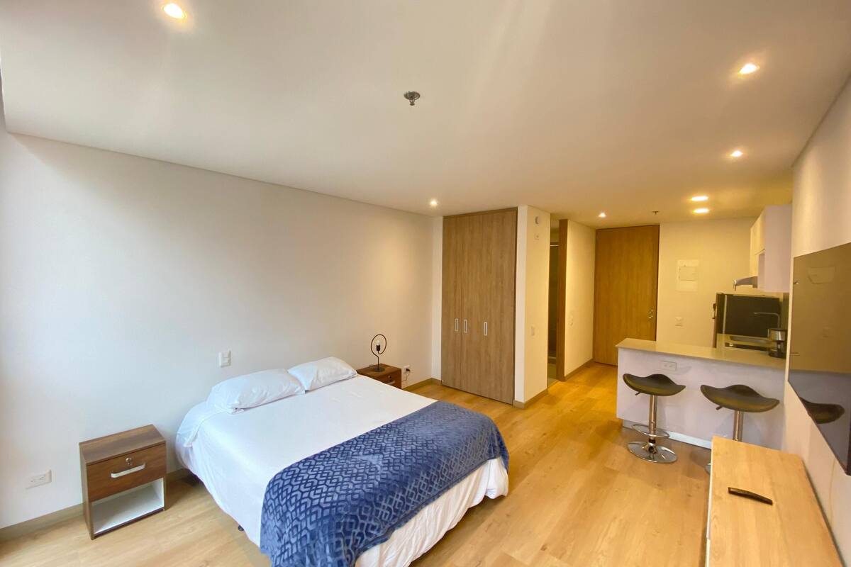 A modern bedroom with a bed, bedside table, and a small desk with stools.