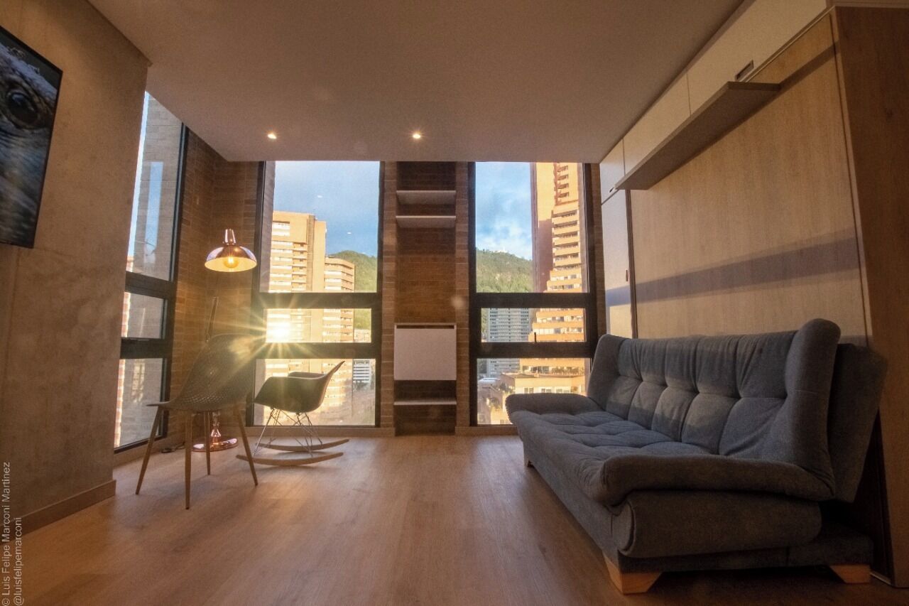 A modern living room with a sofa, a rocking chair, and large windows offering a city view.