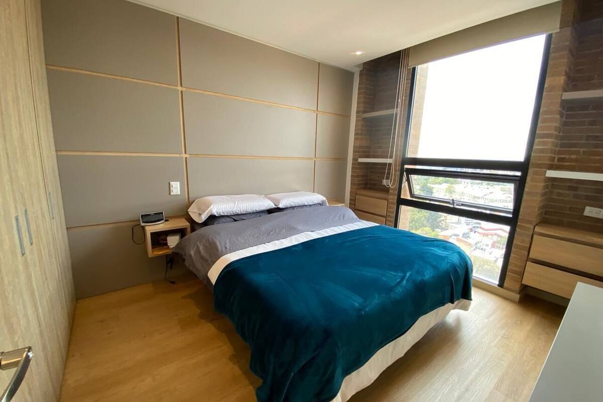 A modern bedroom with a bed, bedside table, and a window with a view.