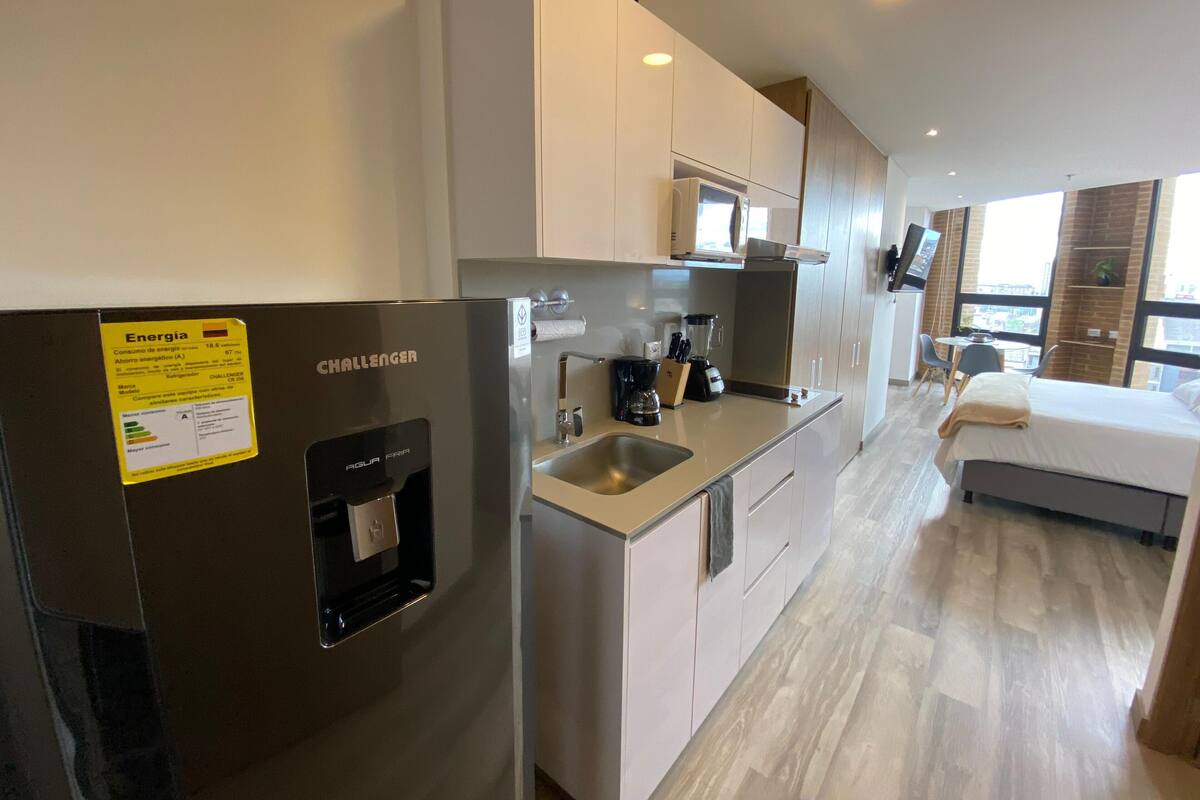A modern kitchen with a refrigerator, coffee maker, and a dining area with a bed.