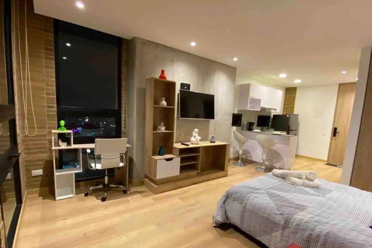 A modern bedroom with a large bed, a desk, and a TV.