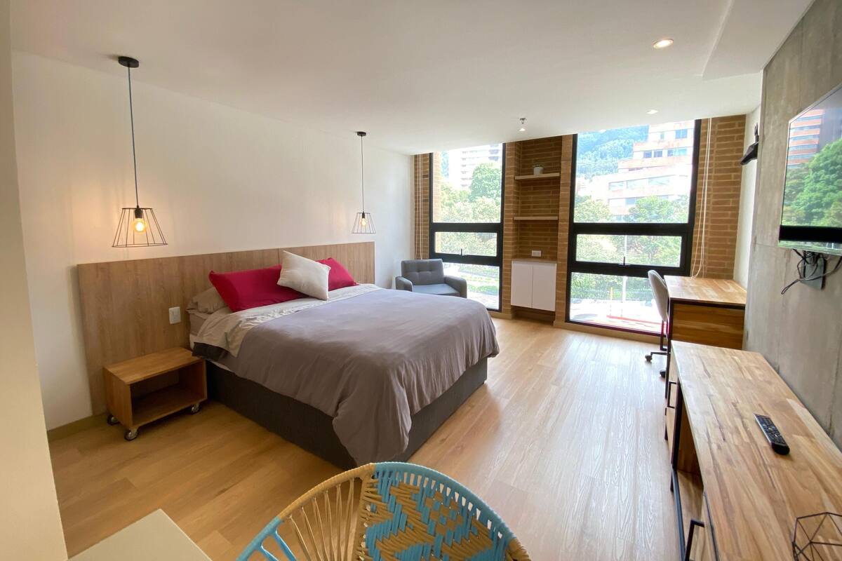 A modern hotel room with a large bed, a desk, and a view of the outdoors.