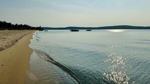 A beach with calm waters, boats, and a clear sky. - Winter Water Woodlands - Hot Tub & Sauna Near Boyne Mountain & Lake Charlevoix (Boyne City)