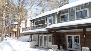 A two-story lodge with a balcony and a stone fireplace. - Winter Water Woodlands - Hot Tub & Sauna Near Boyne Mountain & Lake Charlevoix (Boyne City)