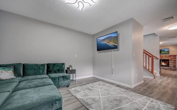 A modern living room with a sectional sofa, a flat-screen TV mounted on the wall, a fireplace, and a staircase leading to another level. - Play : Hike : Swim : Relax : Remote-office :: Best staycation in Pocono (Long Pond)