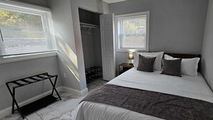 Ein Schlafzimmer mit einem Bett, zwei Fenstern, einem Nachttisch, einer Lampe und einem Schuhregal.