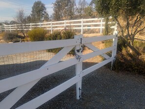 A white metal gate with a lock, set in a gravel area with a white fence and trees in the background. - The Wine Ranch is close to wineries, horses, soccer and pet friendly. (Temecula)