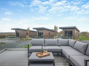 A modern outdoor seating area with a sectional sofa and a wooden tray table. - Lligwy Lodge 3 - UK42793 (Llangefni)