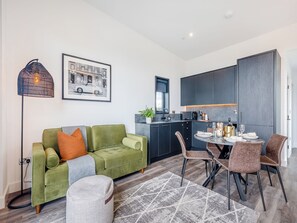 A modern living room with a green sofa, a dining table with chairs, a kitchen area, and a framed picture on the wall. - Lligwy Lodge 3 - UK42793 (Llangefni)