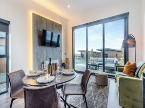 A modern dining area with a round table, chairs, and a flat-screen TV mounted on the wall. - Lligwy Lodge 3 - UK42793 (Llangefni)