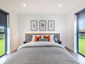 A modern bedroom with a large bed, framed botanical prints on the wall, and a view of greenery outside. - Lligwy Lodge 3 - UK42793 (Llangefni)