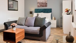 Un dormitorio moderno con un sofá gris, una mesita de madera, una cama con cabecero color turquesa y una mesita de noche con lámpara.