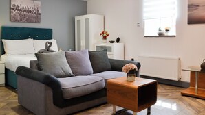 Una sala moderna con un sofá gris, una mesa de centro de madera y una cama con cabecera turquesa.