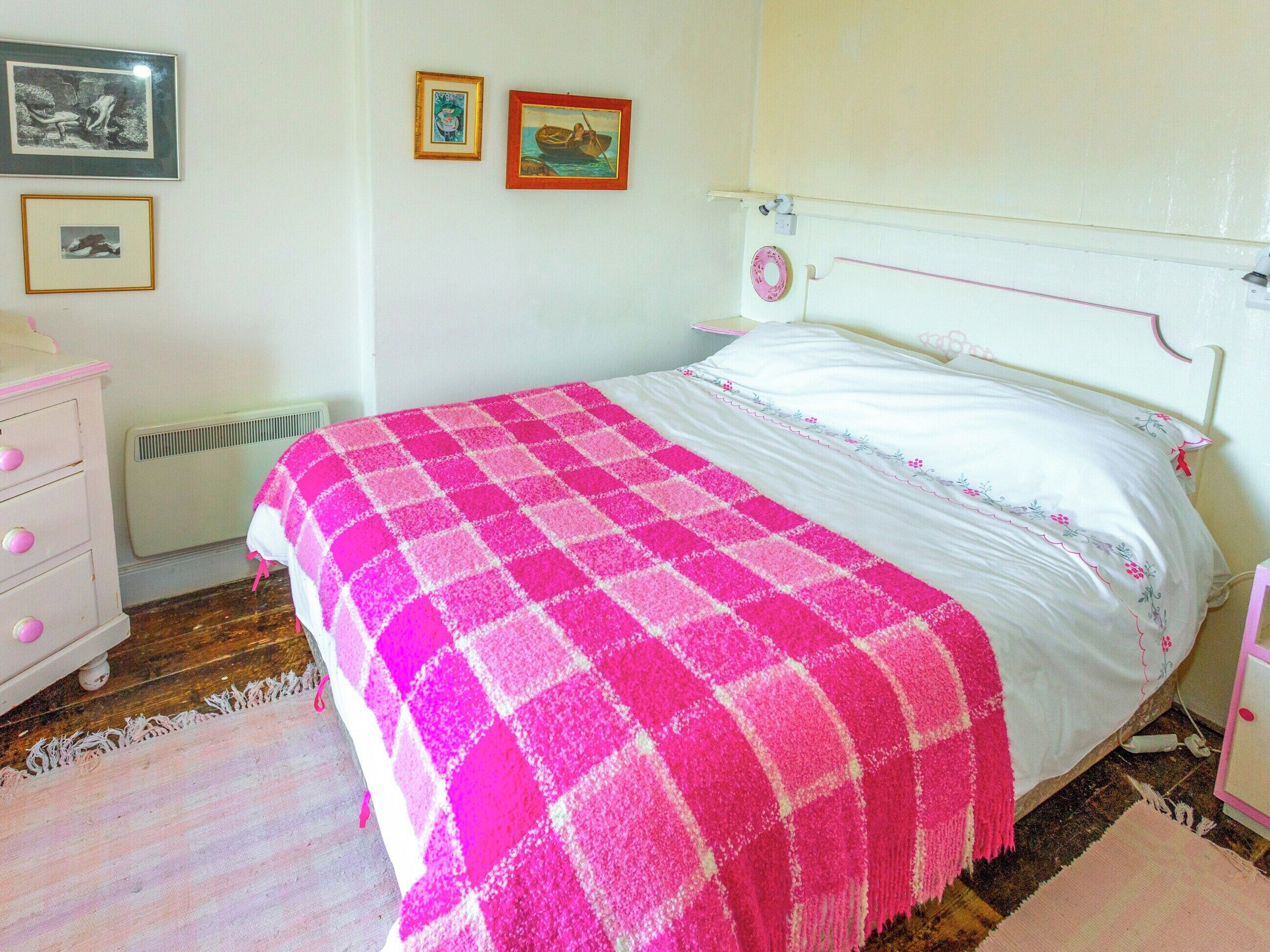 A bedroom with a bed, a dresser, a radiator, and framed pictures on the wall.