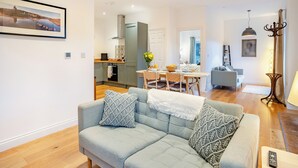 A modern living room with a sofa, a dining area, and a kitchen in the background.