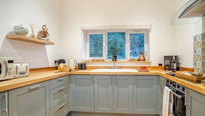 A modern kitchen with grey cabinets, a wooden countertop, a sink, a stove, and a window with a view of trees.