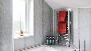 Et moderne badeværelse med et stort badekar, et vindue med udsigt og en håndklædestang med røde håndklæder.