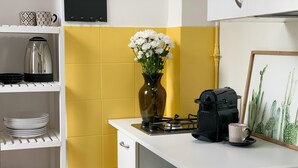 Eine Küche mit gelber Spritzschutzwand, einer Kaffeemaschine, einer Vase mit Blumen und einem Bild von einer Kaktee in einem Rahmen.
