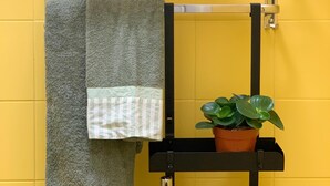 Ein Badezimmer mit einer gelben Wand, einem Handtuchhalter mit einem gelben Handtuch, einem grauen Handtuch und einem Blumentopf.