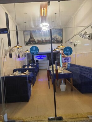 A restaurant with blue upholstered booths, a central counter, and a cityscape mural on the wall. - Dhaka Guest House (Phnom Penh)