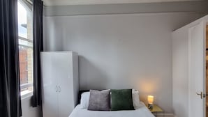 Une chambre d’hôtel avec un grand lit, une armoire, une table de chevet avec une lampe et une fenêtre avec des rideaux.