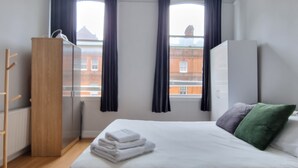 Une chambre d’hôtel avec un lit, une armoire, un bureau et une vue sur les bâtiments par la fenêtre.
